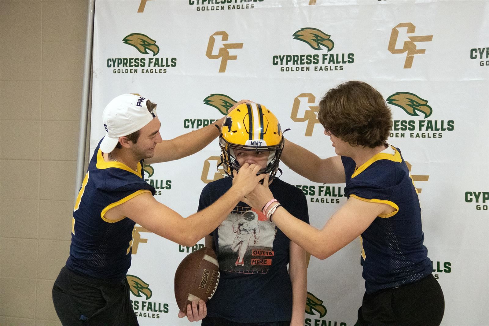 Cypress Ranch High School football players help a Camp Courage participate adjust a football helmet for a photo.